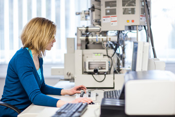 Pretty, female researcher using a microscope in a lab, doing res