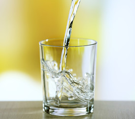 Pouring water from bottle on  glass on light background