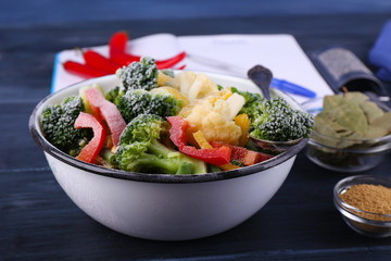 Frozen vegetables and blank notebook, on wooden table