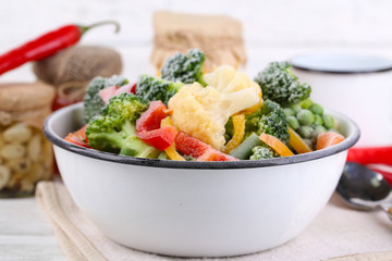 Frozen vegetables in bowl on napkin, on wooden table background
