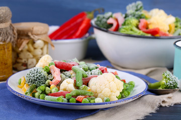 Frozen vegetables on plate on napkin, on wooden table