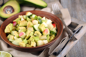 Salad with apple and avocado in bowl on tray on table close up