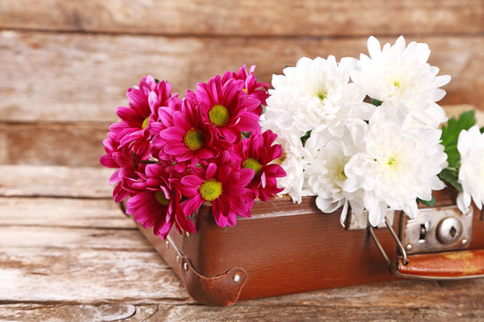 Old wooden suitcase and flowers on wooden background