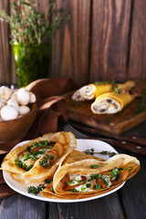 Pancakes with creamy mushrooms on wooden background