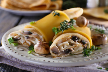 Pancakes with creamy mushrooms in plate on wooden table,