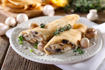 Pancakes with creamy mushrooms in plate on wooden table,