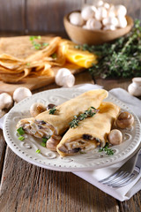 Pancakes with creamy mushrooms in plate on wooden background