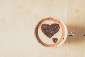 Heart shape on coffee cup on wooden background with vintage colo