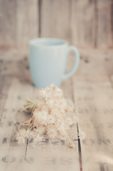 Bouquet of dried flowers and tea cup on wooded background.