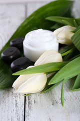 Cosmetic cream with flowers and spa stones on wooden background