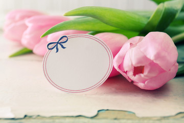 Beautiful pink tulips with tag on wooden background