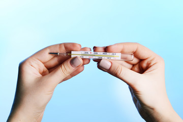 Female hands holding thermometer on blue background