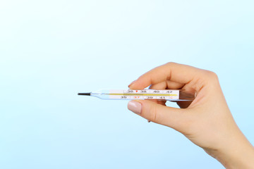 Female hand holding thermometer on blue background