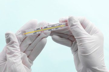 Hands with gloves holding thermometer on blue background