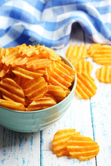 Delicious potato chips in bowl on wooden table close-up