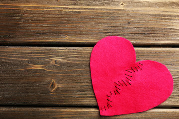 Broken heart stitched from two pieces on wooden background