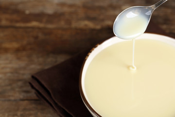 Bowl with condensed milk on napkin on wooden background
