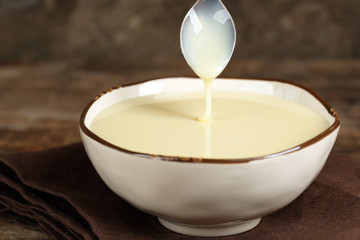 Bowl with condensed milk on napkin on wooden background