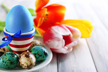 Easter egg in holder and tulip flowers on wooden background
