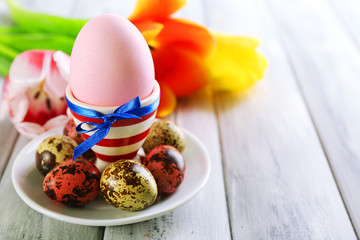 Easter egg in holder and tulip flowers on wooden background