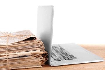 Laptop with stack of newspapers on table isolated on white