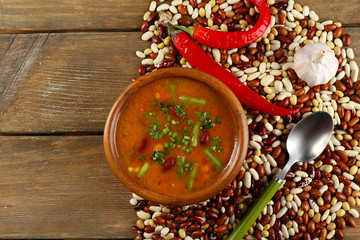 Bean soup in bowl and raw beans on wooden table background