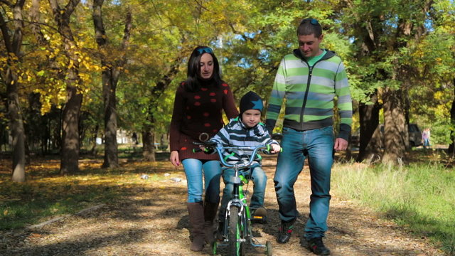 Happy Young Family With a Child On Bike Walking In Autumn Park