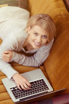 moderne frau liegt mit laptop auf einem gelben sofa