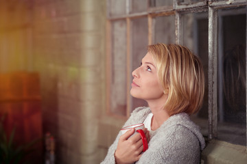 blonde frau lehnt am fenster und schaut nach oben