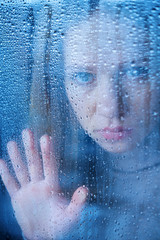 melancholy and sad young  woman  at the window in the rain