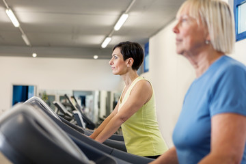 Fototapeta na wymiar Two mature women are running on a treadmill