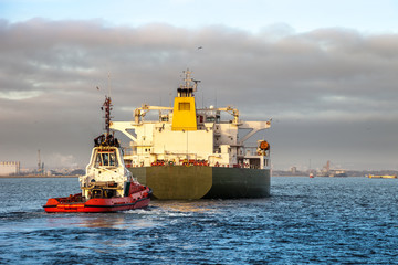 Tanker ship with escorting tug in port.