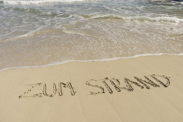 Fototapeta na wymiar Text ZUM STRAND am Sandstrand mit Wellen