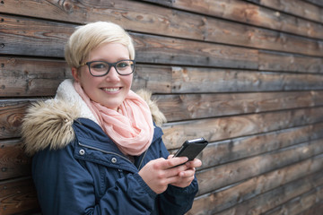 Smiling Young Woman with Smartphone leaning at a wall