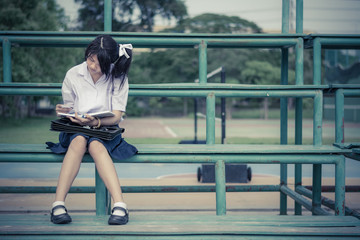 Cute Thai schoolgirl is sitting and reading on a stand in vintag