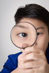 portrait of a young asian child looking through a magnifying gla