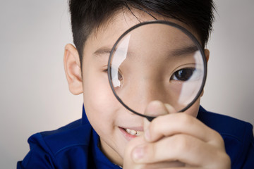 portrait of a young asian child looking through a magnifying gla