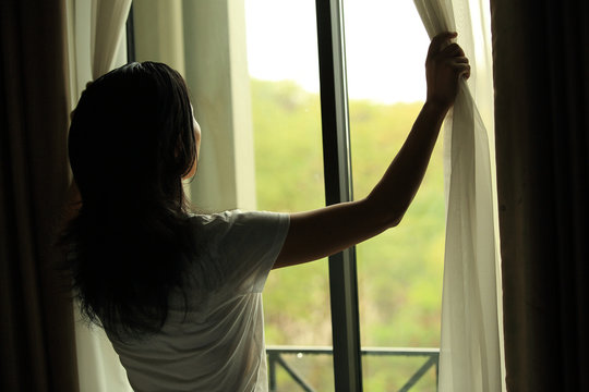 girl opening curtains in a bedroom