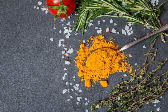 spoons with turmeric and herbs on  black