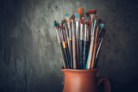 Image of Collection of artists paintbrushes in jar beside paint pots -  Austockphoto