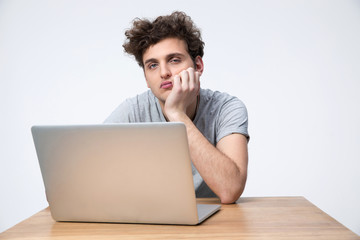 Tired man sitting at the table with laptop over gray background