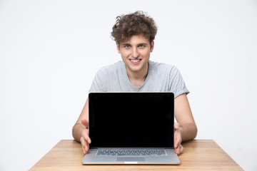 Cheerful man sitting at the table and showing laptop screen