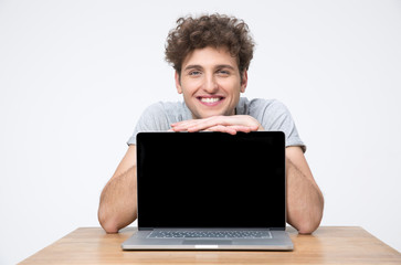 Happy man sitting at the table and showing laptop screen