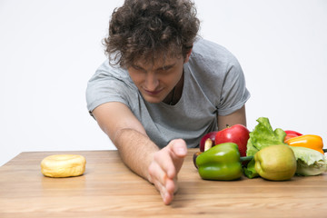 Fototapeta premium Young man choosing healthy vegetables food or unhealthy donut