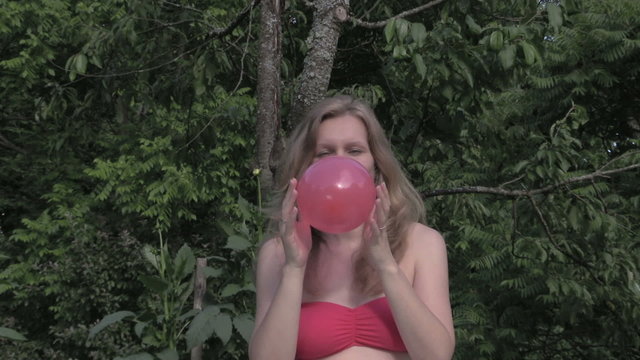 pregnant woman blow balloon in sit on plaid in green garden