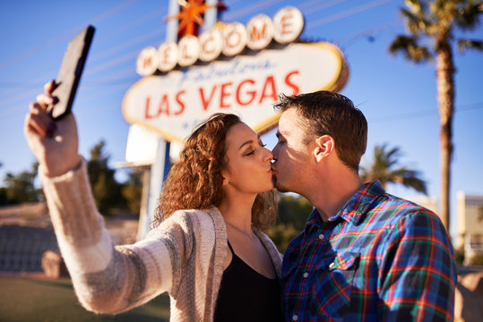 couple kissing and taking selfie by welcome to las vegas sign
