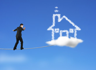 Businessman walking on rope toward house shape cloud in sky