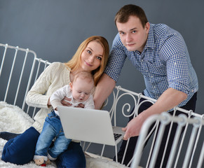 Mother ,father with baby and laptop sitting on bed