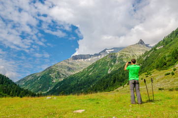 Young mountaineer taking a photo of alpine landscape, Alps