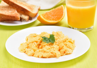 Scrambled eggs on white plate, toast and orange juice